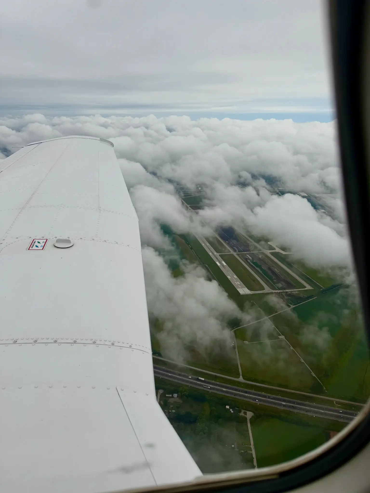 Airplane wing seen from cockpit window during flight above clouds