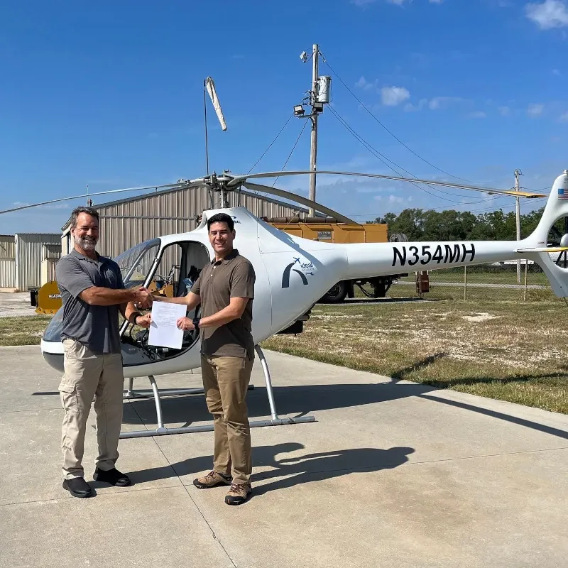 Student and CFI shacking hands with certificate in hand in front of a helicopter