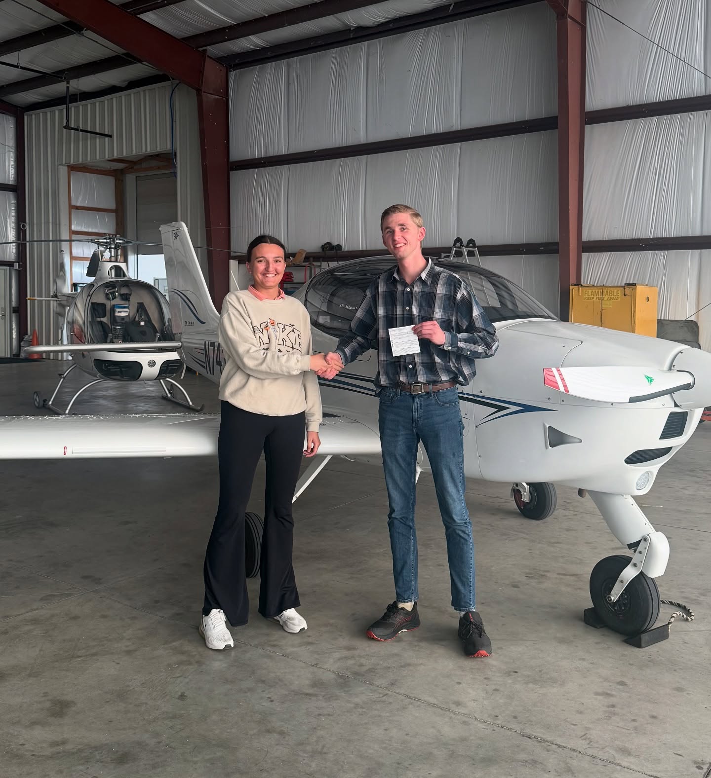 Instructor and student smiling and shaking hands while holding a certificate in front of an aircraft